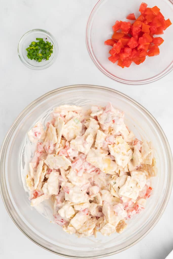Large bowl of tomato cracker salad, with small bowls of chopped chives and diced tomatoes on a white surface.