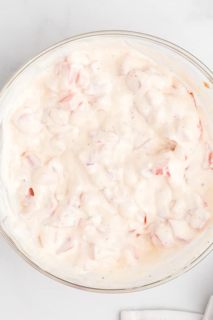 A bowl of mayonnaise mixed with chopped tomatoes, seen from above on a white surface.
