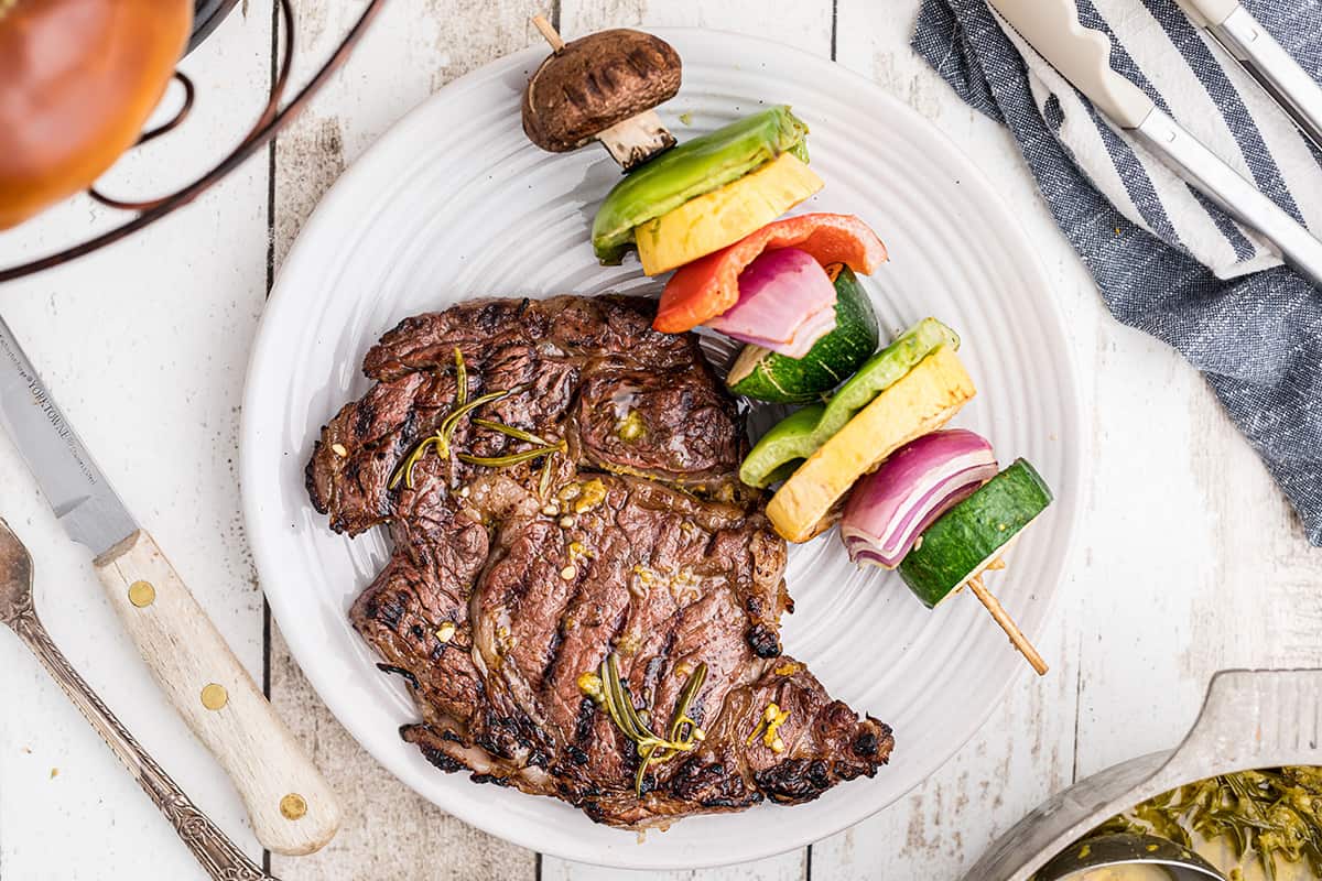 A cooked steak on a plate with a skewer of veggies.