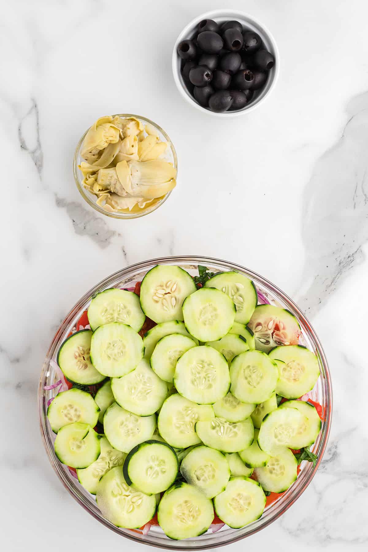 Sliced cucumbers layered into the salad bowl.