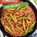 A skillet filled with southern stewed okra and tomatoes, garnished with seasoning, shown on a wooden surface with a checkered cloth nearby.