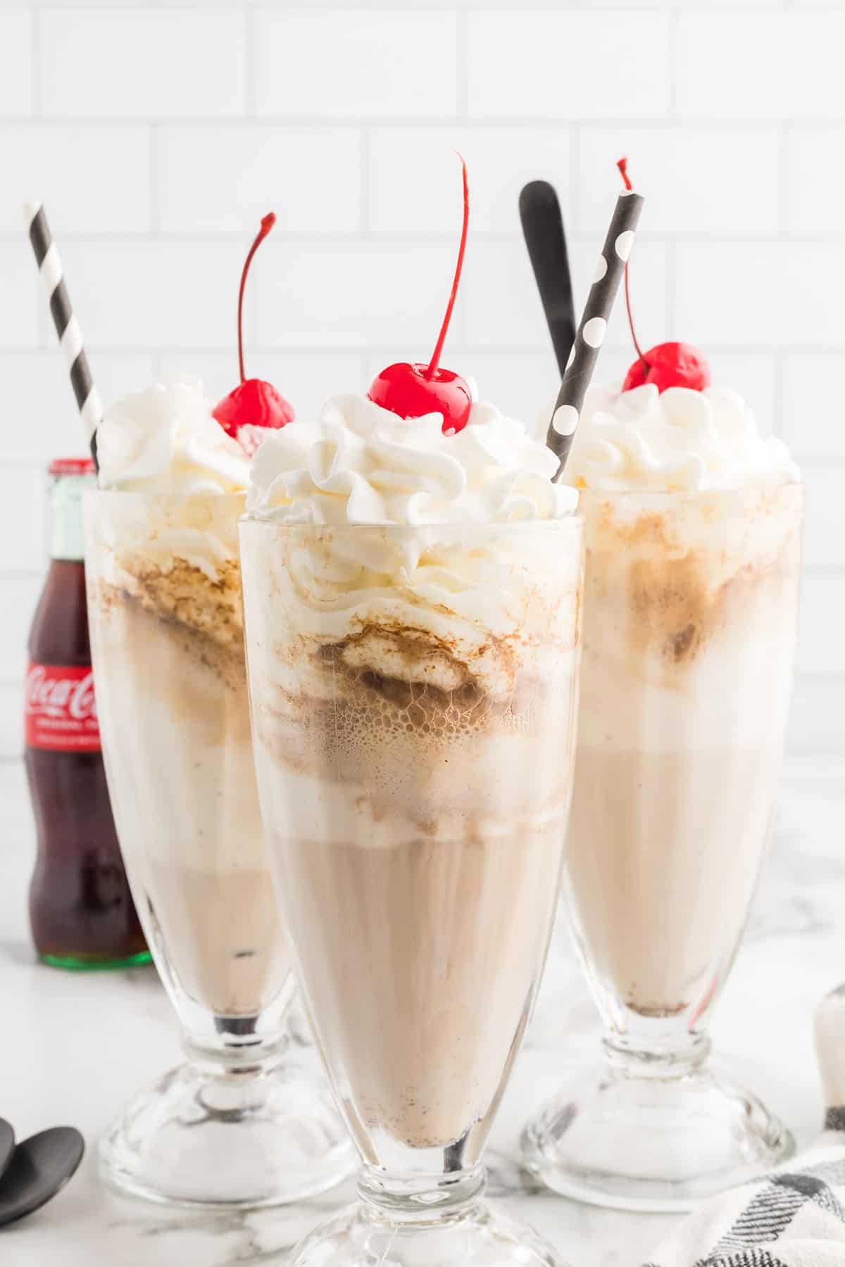 Coke floats in tall glasses with whipped cream and a cherry on top.