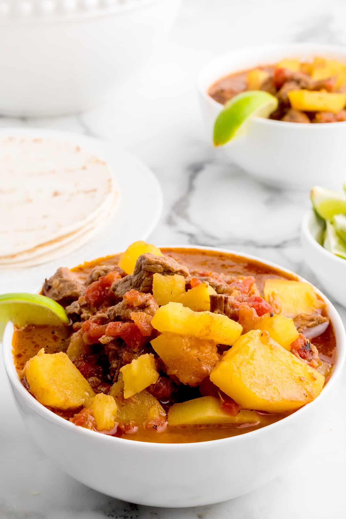 A bowl of Mexican beef stew with lime wedges on the side.