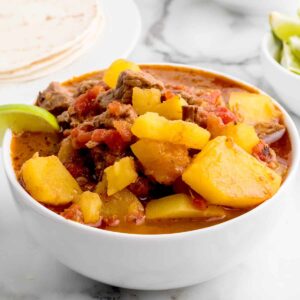 A bowl of Mexican beef stew with lime wedges on the side.