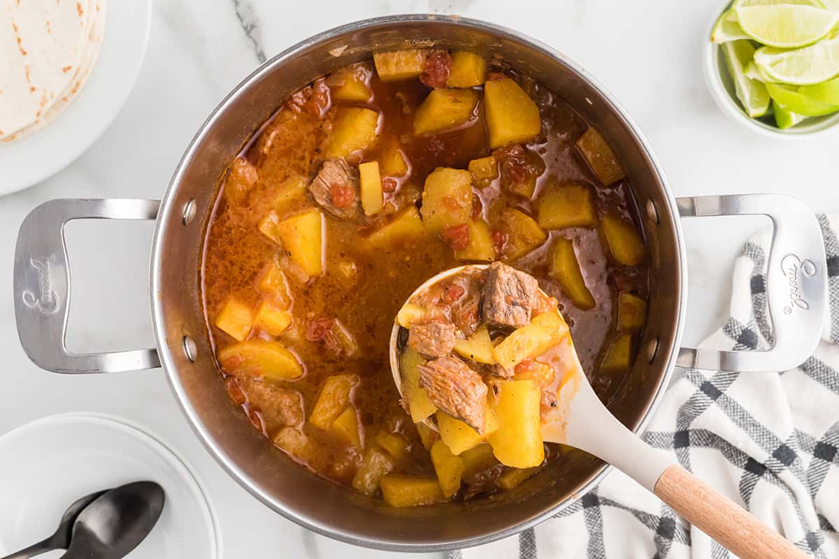 A spoonful of Mexican beef stew suspended above the cooking pot.