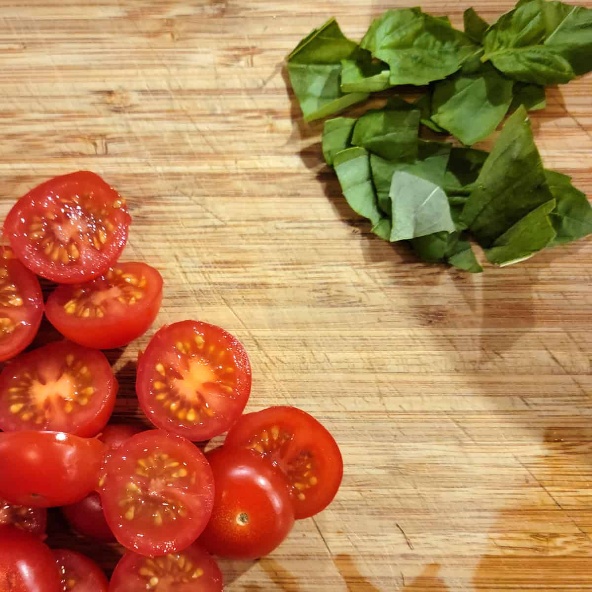Prepared cherry tomatoes and basil leaves on a cutting board.