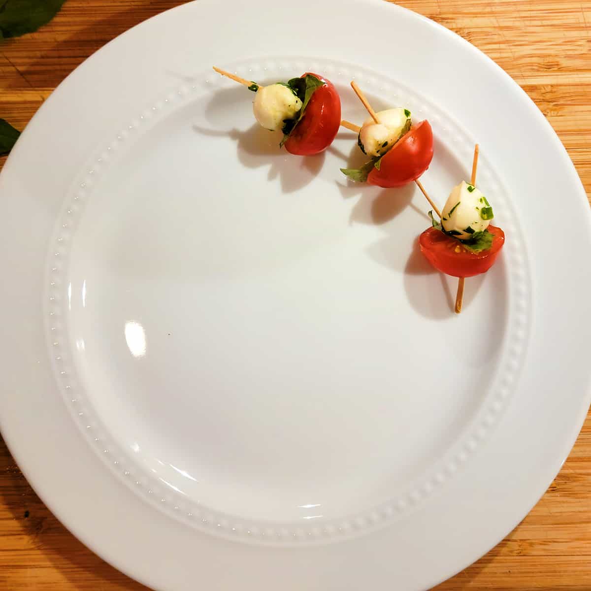 Assembling the caprese skewers on a white plate.