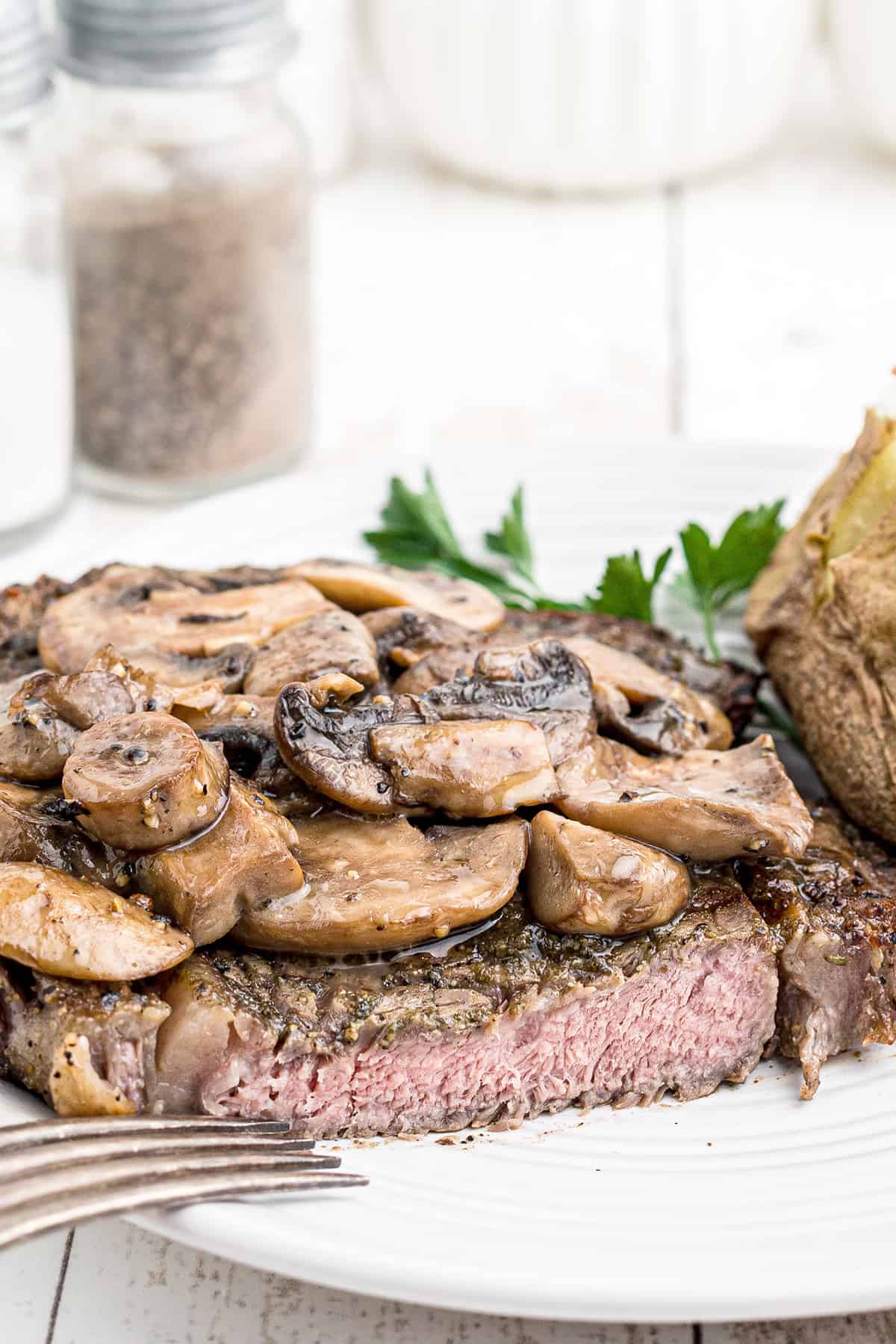 A ribeye steak with baked potatoes and mushrooms on a white plate.