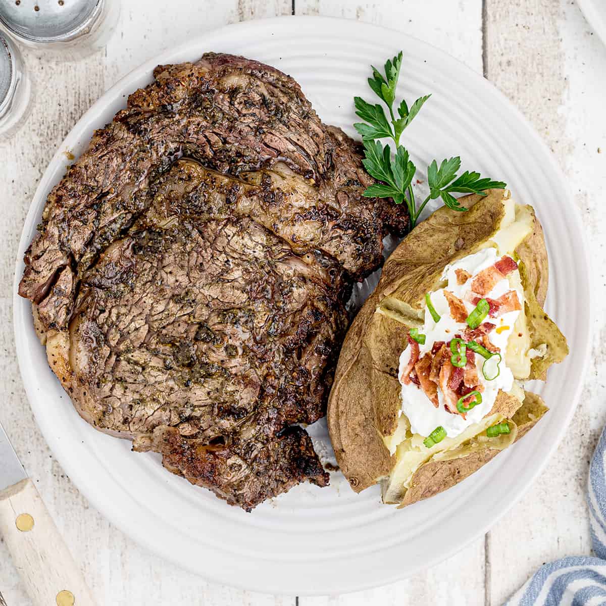 A ribeye steak with baked potato on a white plate.