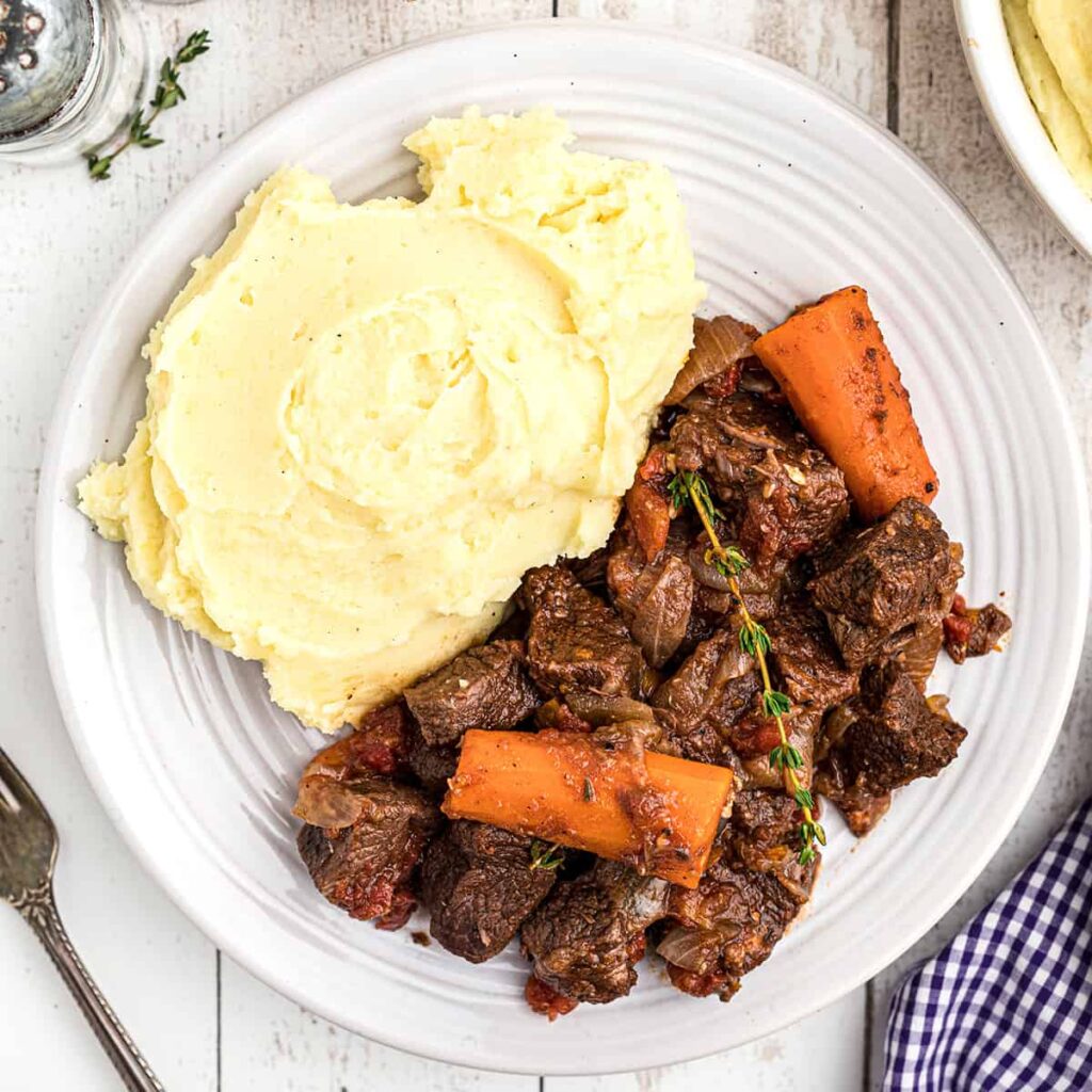 Beef stew on a plate alongside mashed potatoes.