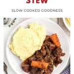 Plate of beef stew with carrots and mashed potatoes, garnished with thyme, on a white table.