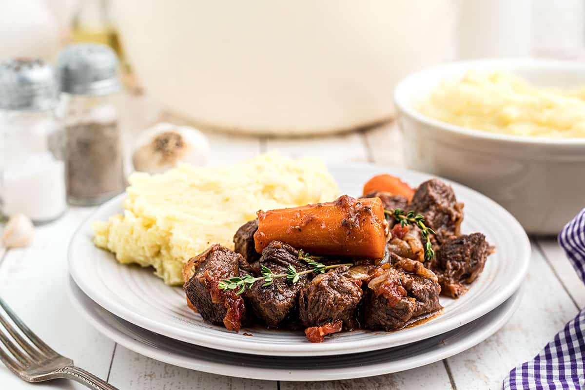 Beef stew on a plate alongside mashed potatoes.
