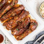 A platter of barbecued ribs with coleslaw and sauce on the side.