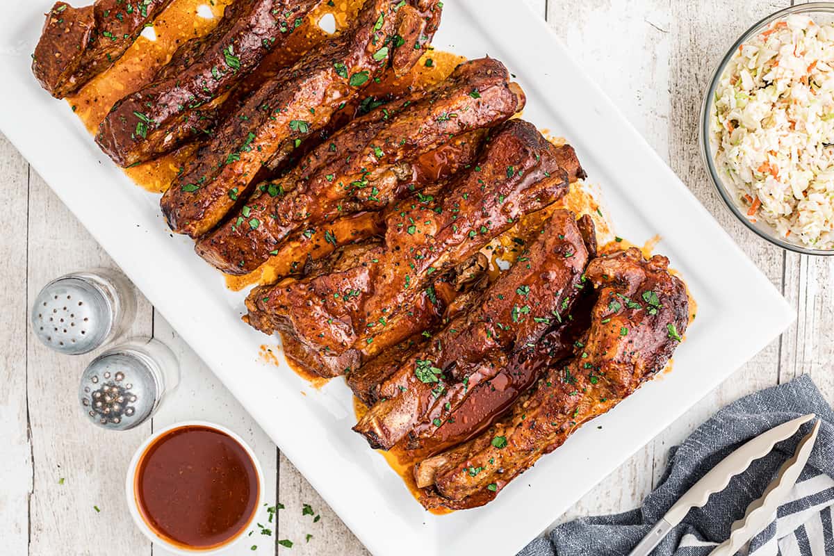 A platter of barbecued ribs with coleslaw and sauce on the side.