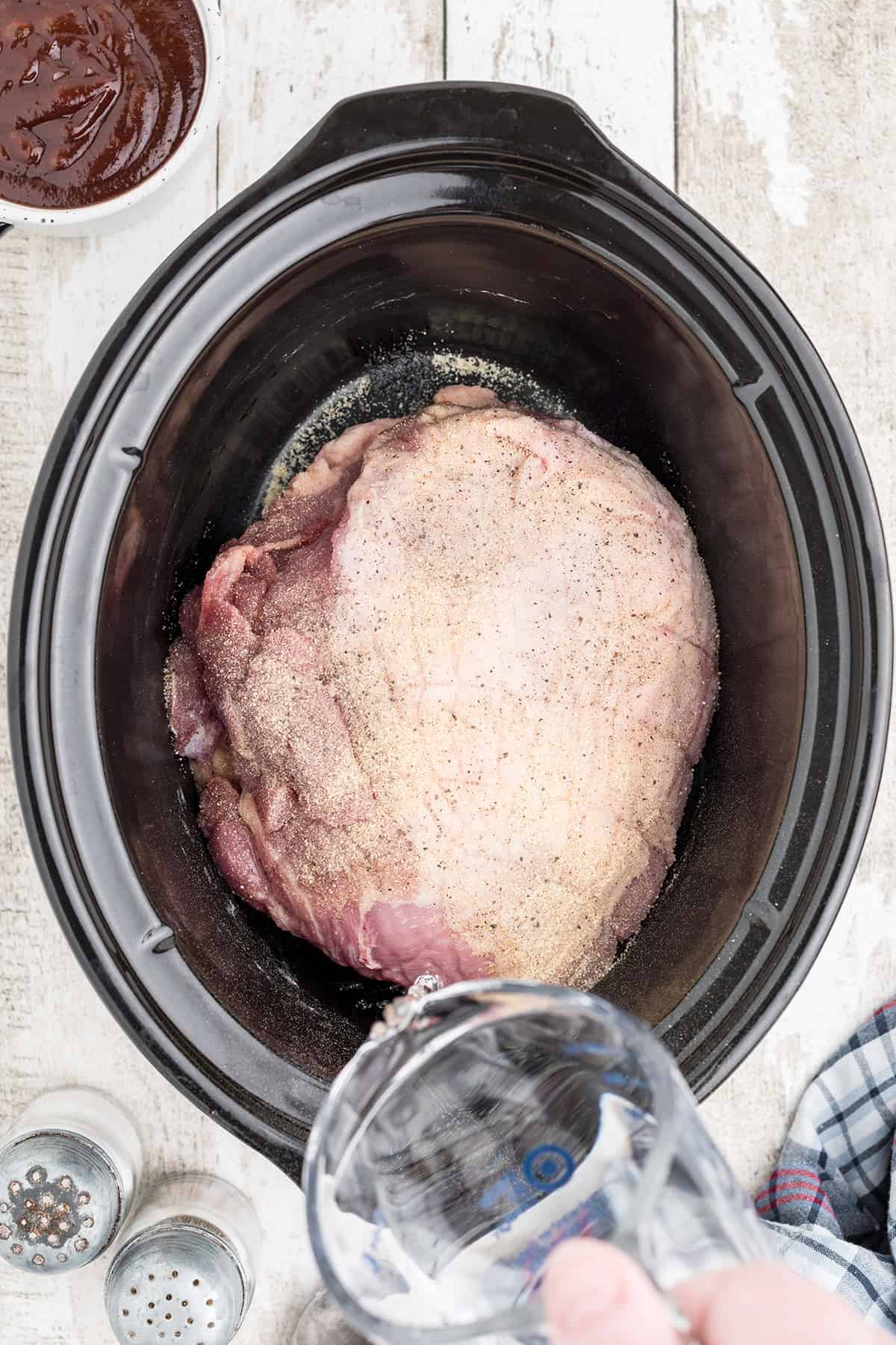 Pouring water into the slow cooker with the pork roast.