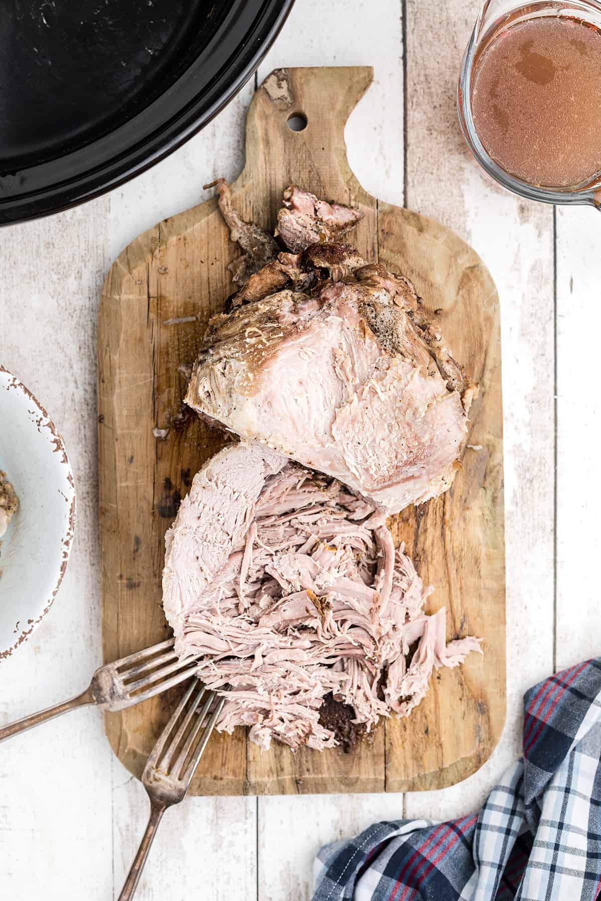 Cooked pork roast being shredded into pieces on a wooden cutting board.