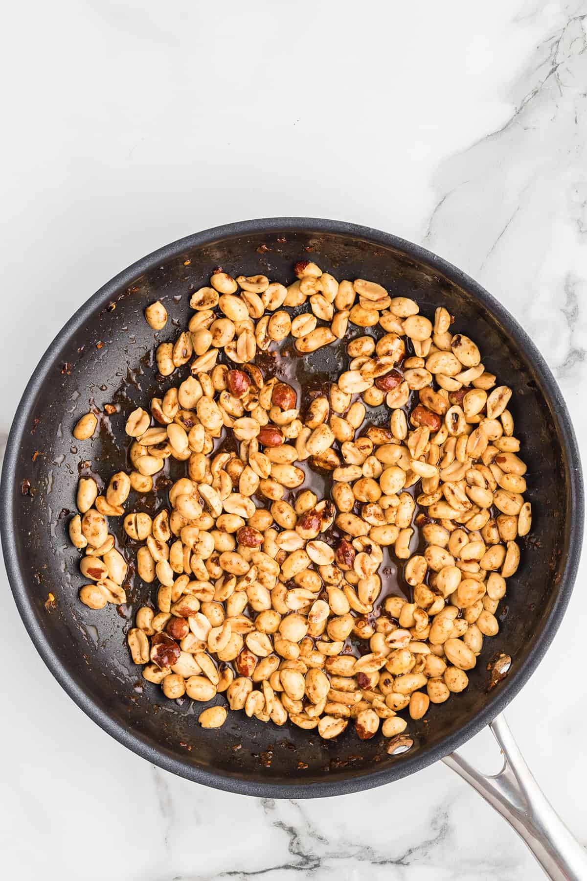 Peanuts and spices cooking in a frying pan.