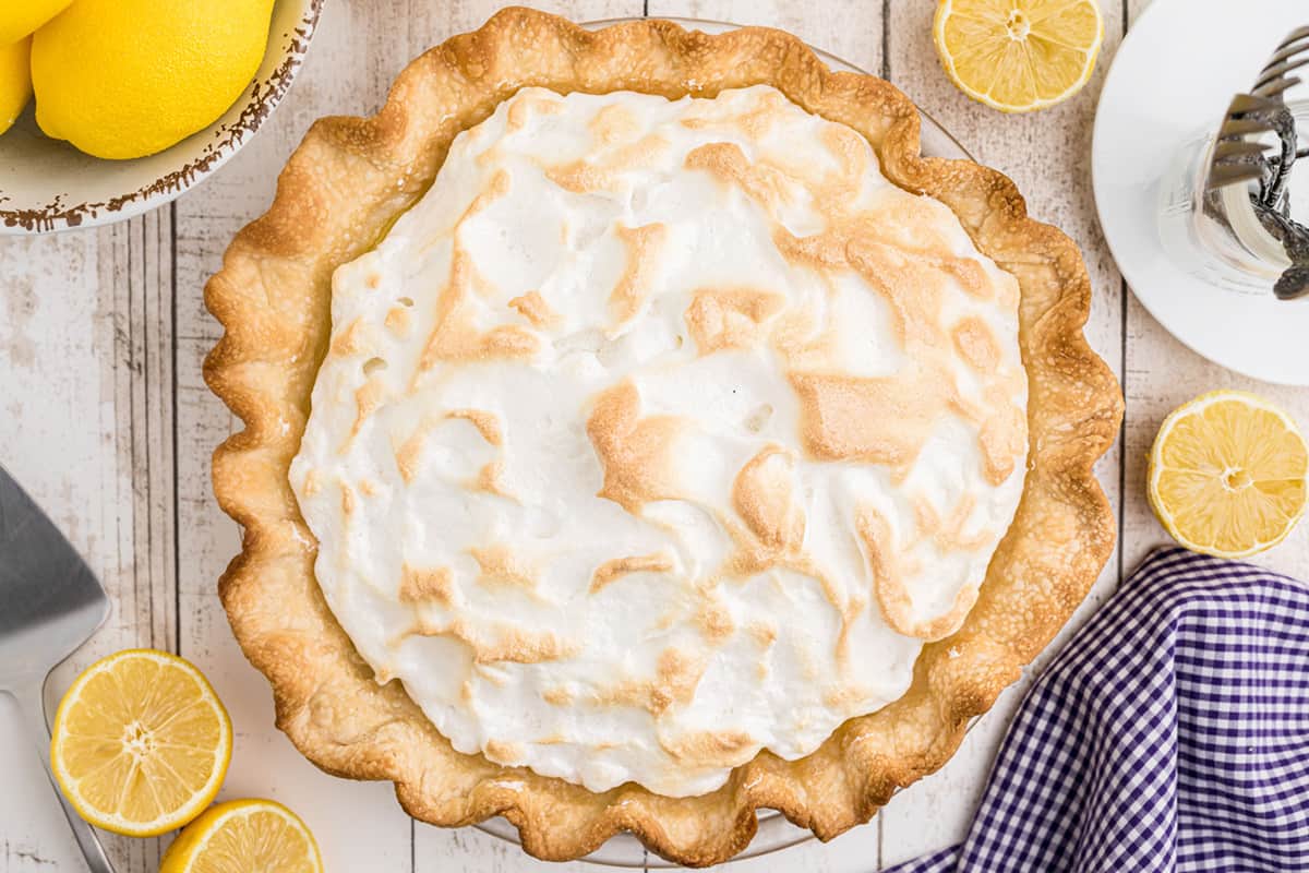 Whole finished lemon meringue pie on a white wood background.
