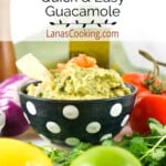 Finished guacamole in a decorative bowl surrounded by ingredients used in the recipe.