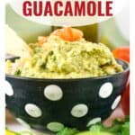 A bowl of homemade guacamole with a chip, topped with diced tomatoes, in a black bowl with white dots.