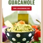A bowl of guacamole with a tortilla chip, surrounded by fresh vegetables and a bottle of oil.