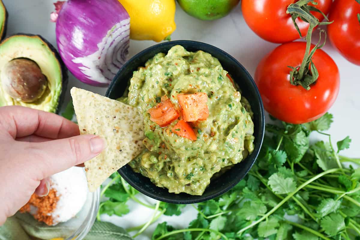 Dipping a chip into finished guacamole in a bowl.