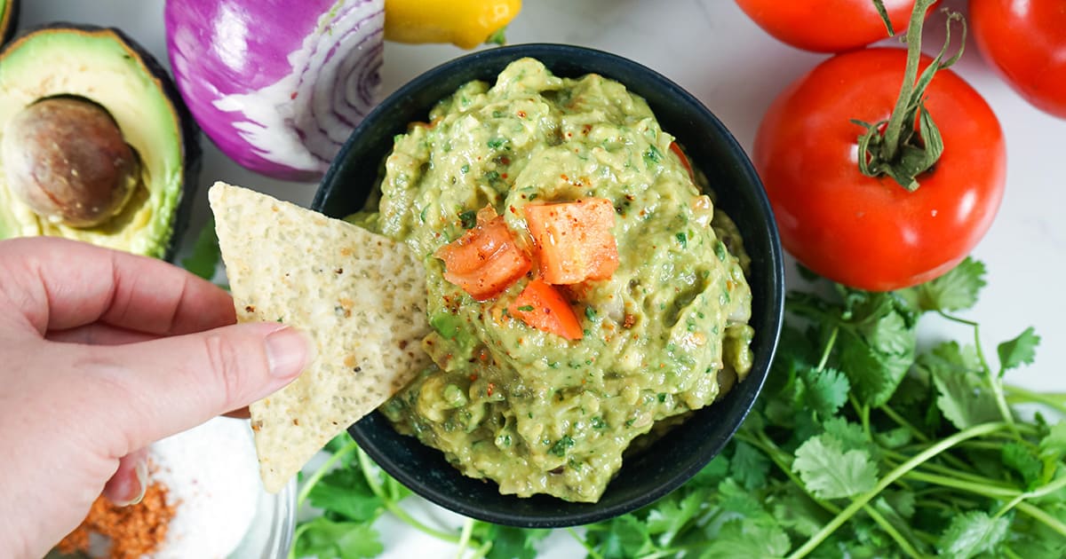 Dipping a chip into finished guacamole in a bowl.