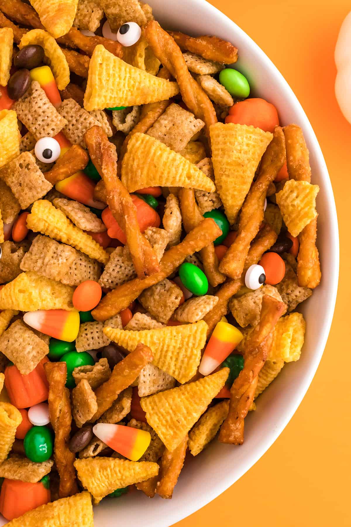A white bowl filled with snack mix sitting on an orange background.