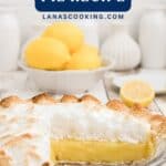 A lemon meringue pie with a slice missing, fresh lemons and kitchen decor in the background.