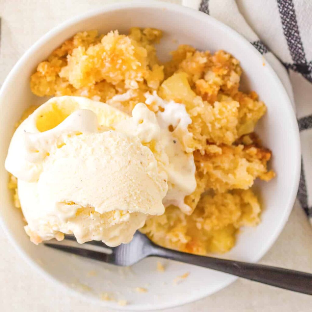 A serving of cobbler in a white bowl with vanilla ice cream on top.