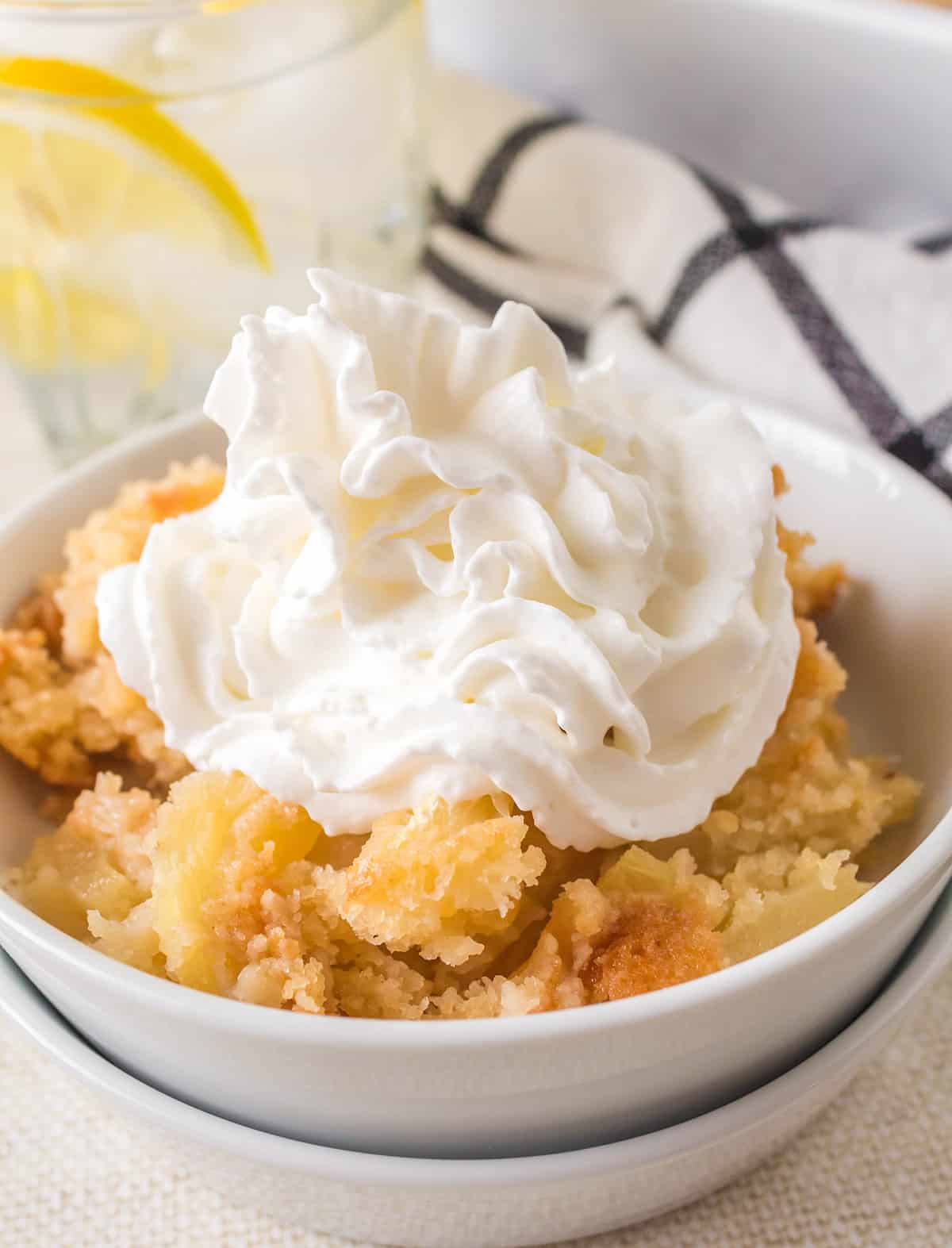 A serving of cobbler in a white bowl with whipped cream on top.