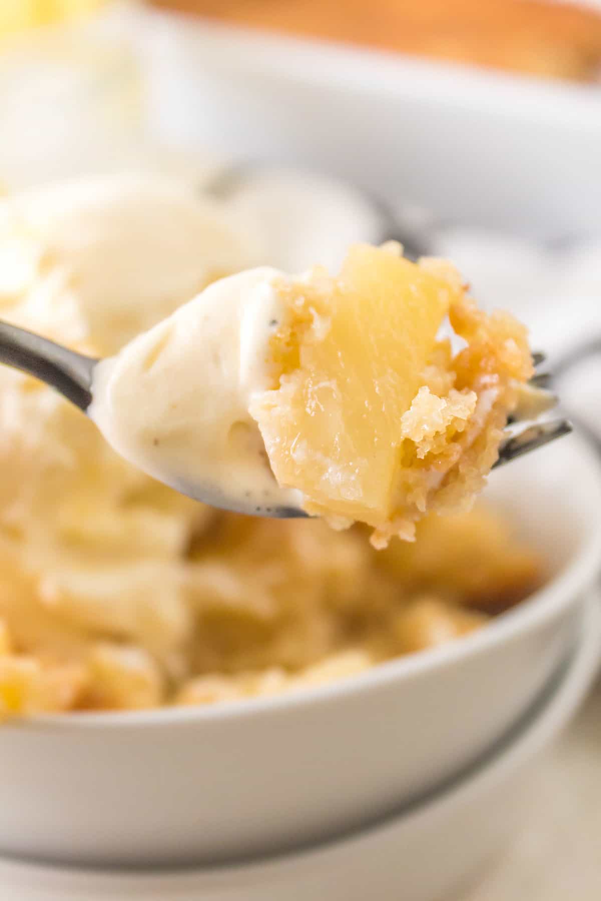 One bite of cobbler on a fork suspended over a serving bowl.