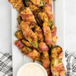 Bacon wrapped jalapeno poppers on a serving platter with a bowl of ranch dressing on the side.