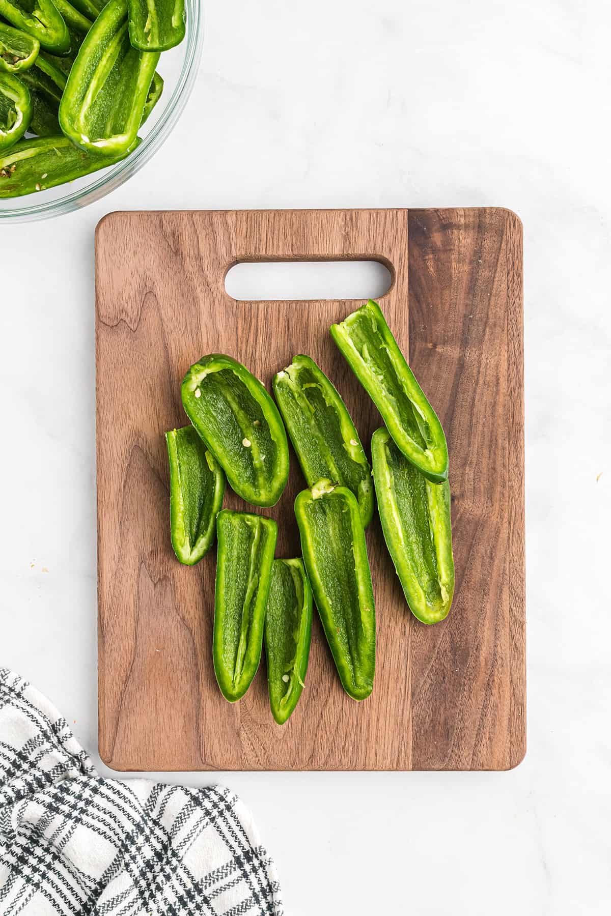 Halved jalapeno peppers on a wooden cutting board.