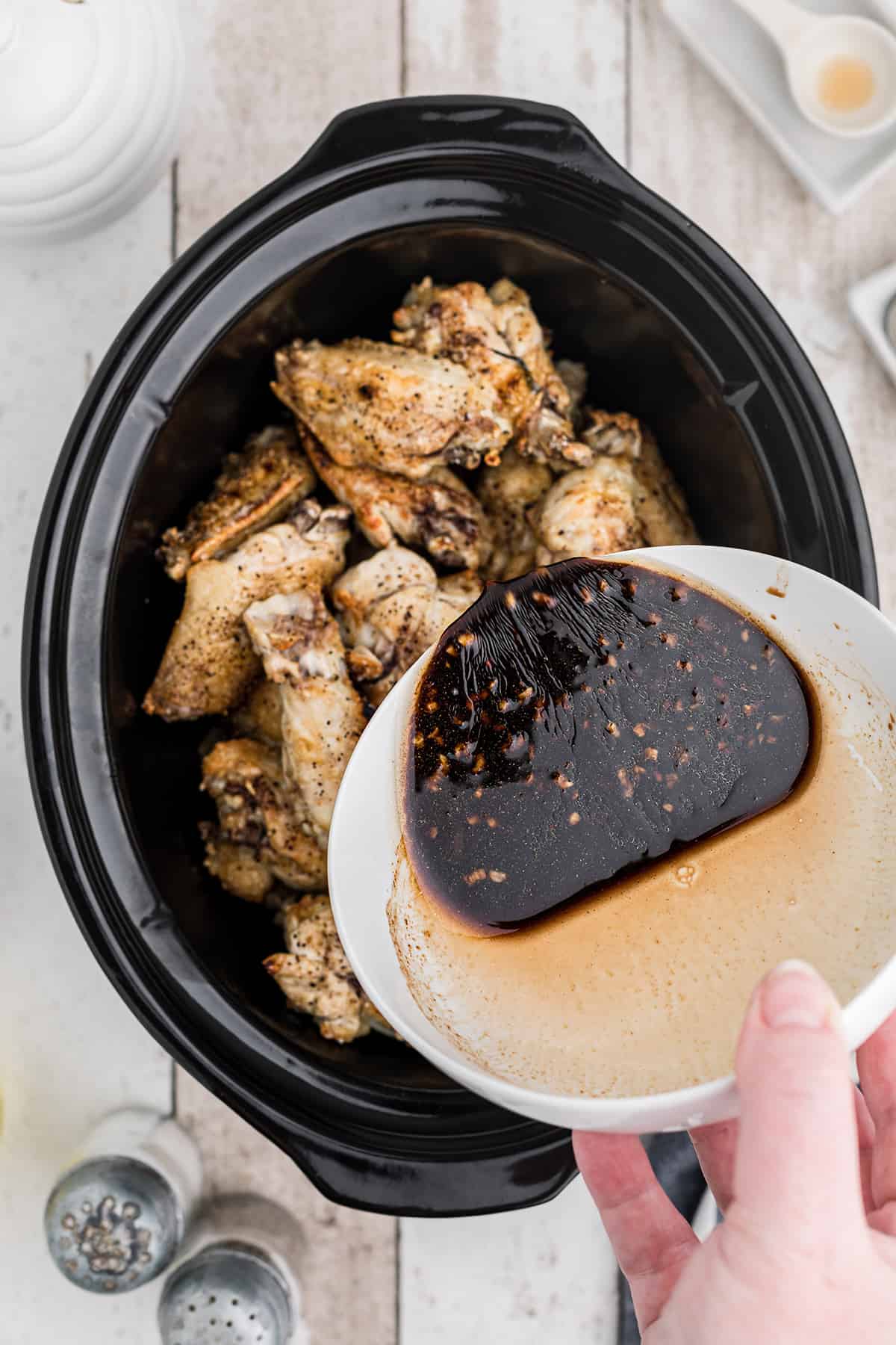 Pouring sauce over the wings in the slow cooker.