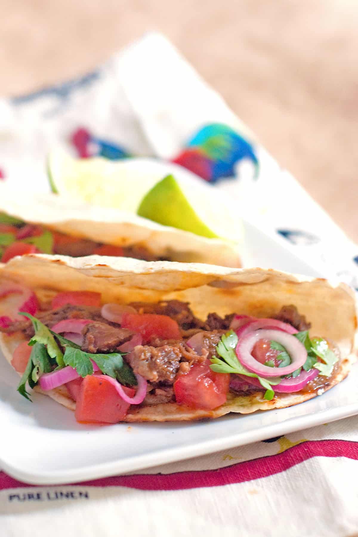 Two slow cooker shredded beef tacos on a serving plate with a kitchen towel underneath.