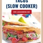 Two shredded beef tacos topped with onions, tomatoes, and cilantro on a white plate with a lime wedge.