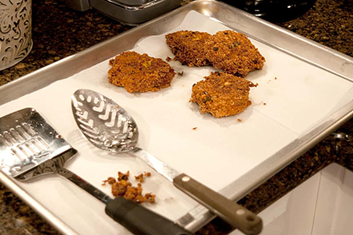 Fritters on paper towels in a baking sheet.