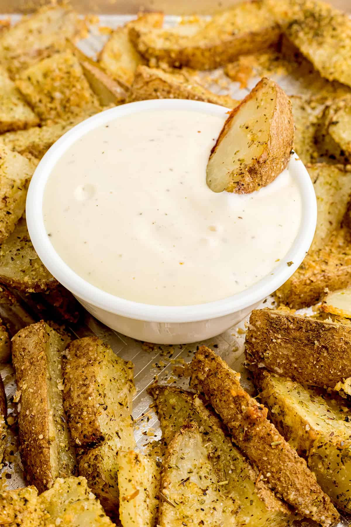 Finished potato wedges on a baking sheet with a bowl of ranch dipping sauce.