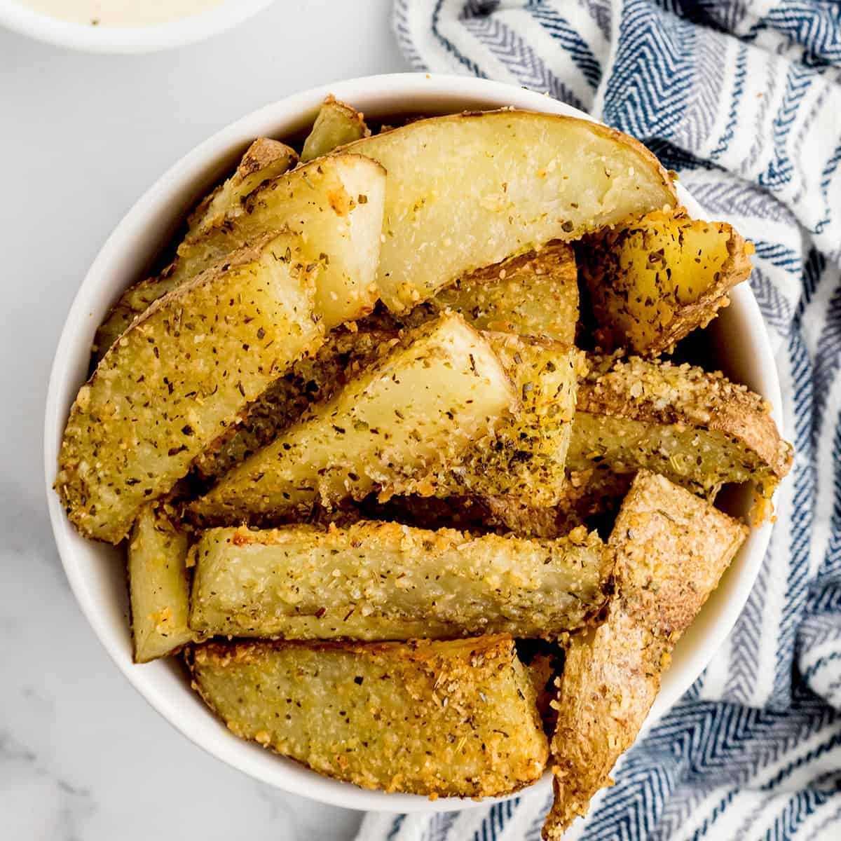 A white bowl containing a serving of crispy baked potato wedges.