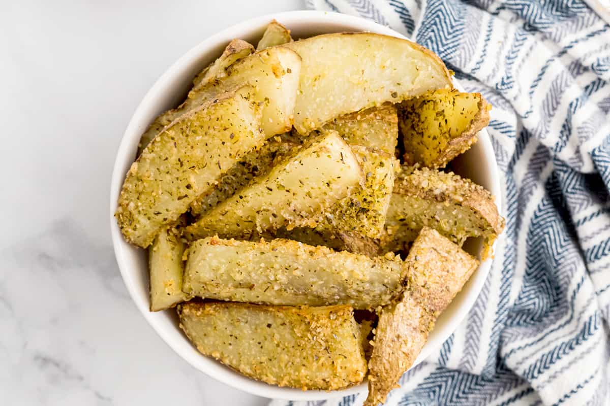 A white bowl containing a serving of crispy baked potato wedges.