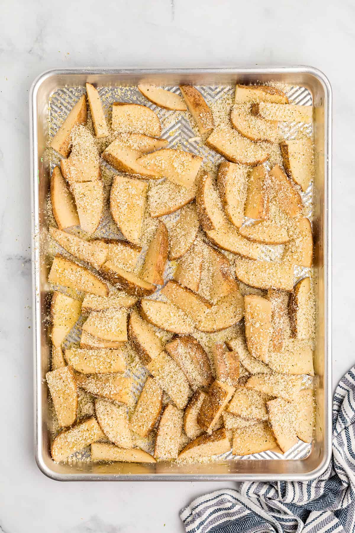 Potato wedges coated with seasoning mixture on a baking sheet.