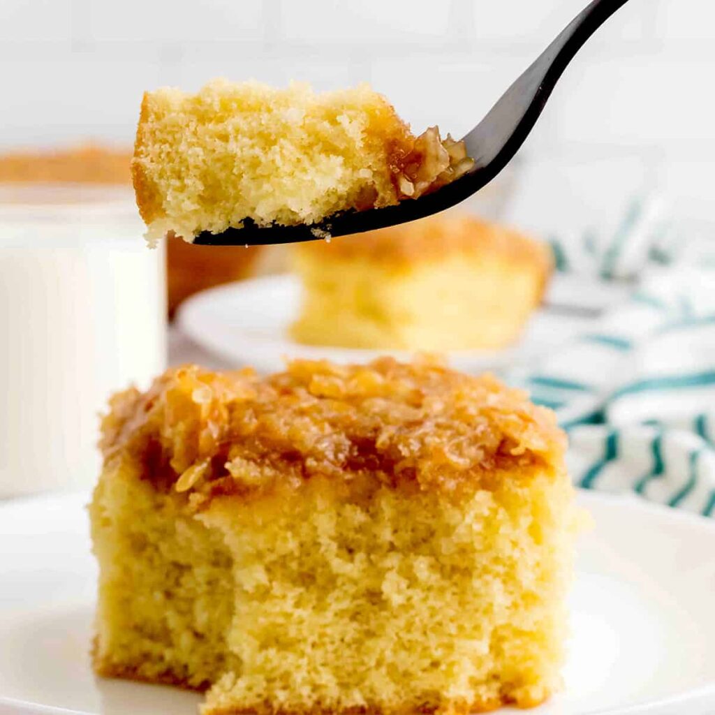 A bite of cake suspended on a fork over a piece of cake on a plate.