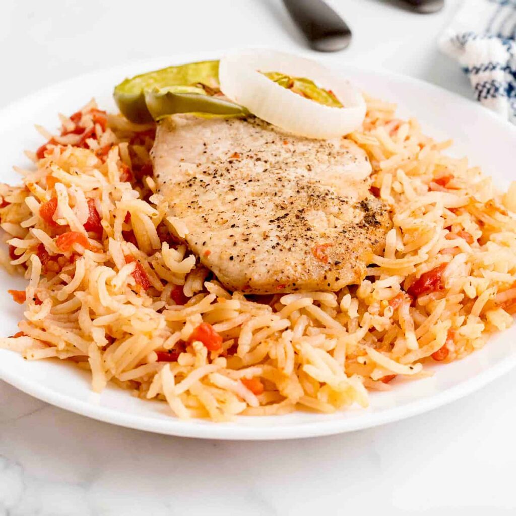 A serving of one dish pork chops and rice on a white plate.