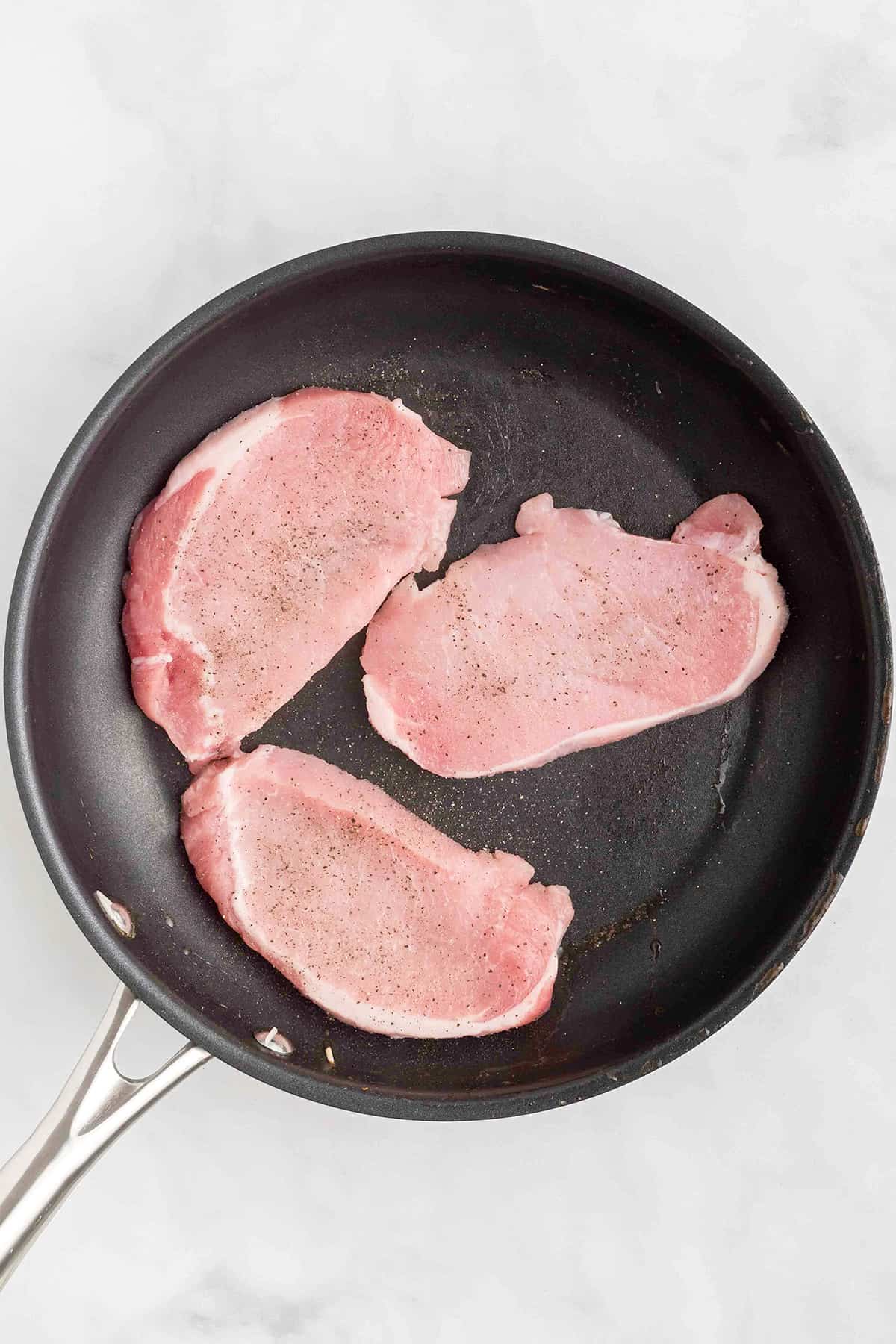 Pork chops in a black skillet.