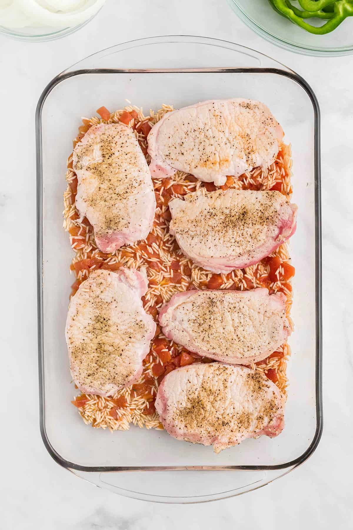 Browned pork chops placed over tomato-rice mixture.