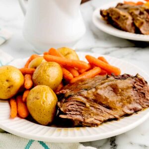 A serving of pot roast with potatoes and carrots on a white plate.