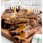 Sliced pot roast with gravy on a wooden board, garnished with herbs, next to a fork and napkin.