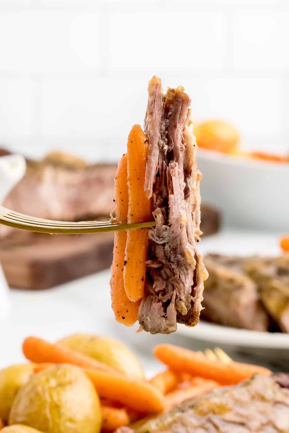 A fork holding a bite of pot roast and carrots.