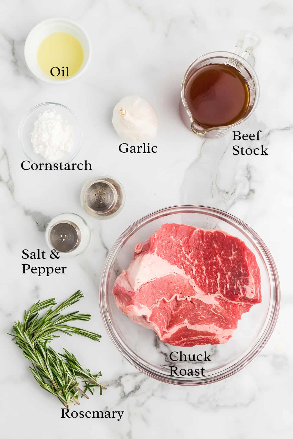 Raw chuck roast, rosemary, cornstarch, oil, garlic, beef stock, salt, and pepper on a marble surface.